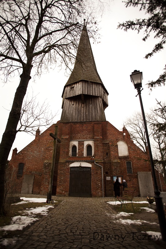 Wejście do kościoła, widok od strony zachodniej, wieża kościelna - na prawo i lewo od drzwi wejściowych, widać przymocowane do ścian kościoła płyty nagrobne - po prawej płyta nagrobna pierwszego proboszcza.